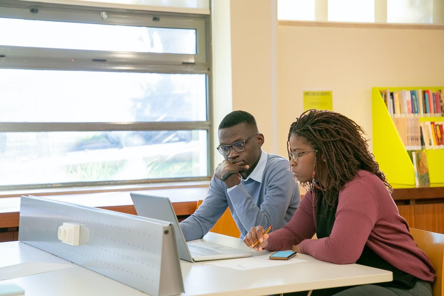 Two learners collaborating with a laptop in a library